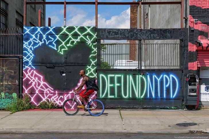 A photo of someone biking past a sign reading "Defund NYPD"